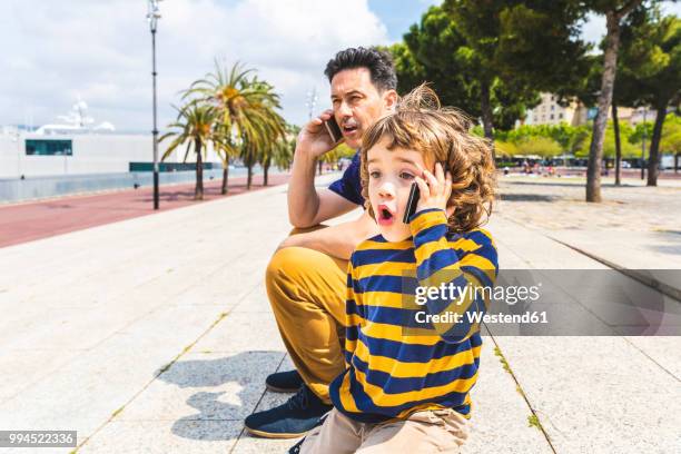 spain, barcelona, father and son both with a smartphone - erwachsene imitieren stock-fotos und bilder