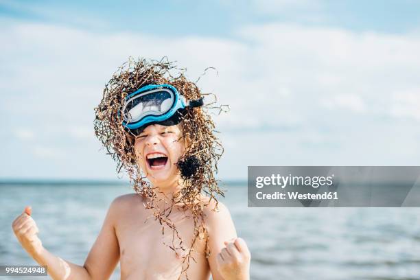 carefree boy wearing seaweed wig on the beach - kust karakteristiek stockfoto's en -beelden