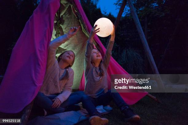 two girls sitting in tipi, holding lamp as moon - all in this together stock-fotos und bilder
