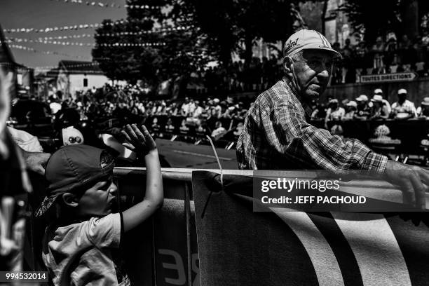 Boy waves and an elderly man looks on as they wait at the start line to watch riders depart for the second stage of the 105th edition of the Tour de...