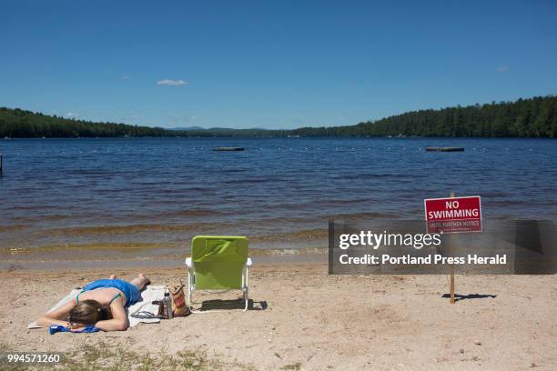 Christy Dow tans on Woods Pond Beach next to one of the no swimming signs that line the sand. Swimming at the popular beach was banned when several...