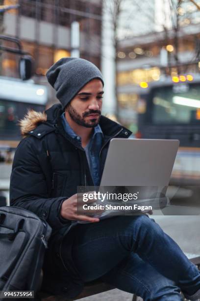 young man using laptop on city street - laptop on bus stock-fotos und bilder
