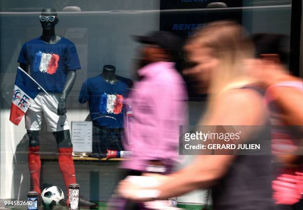 People pass by shop windows displaying outfits of French national football team on July 9, 2018 in Paris, on the eve of France's Russia 2018 World...