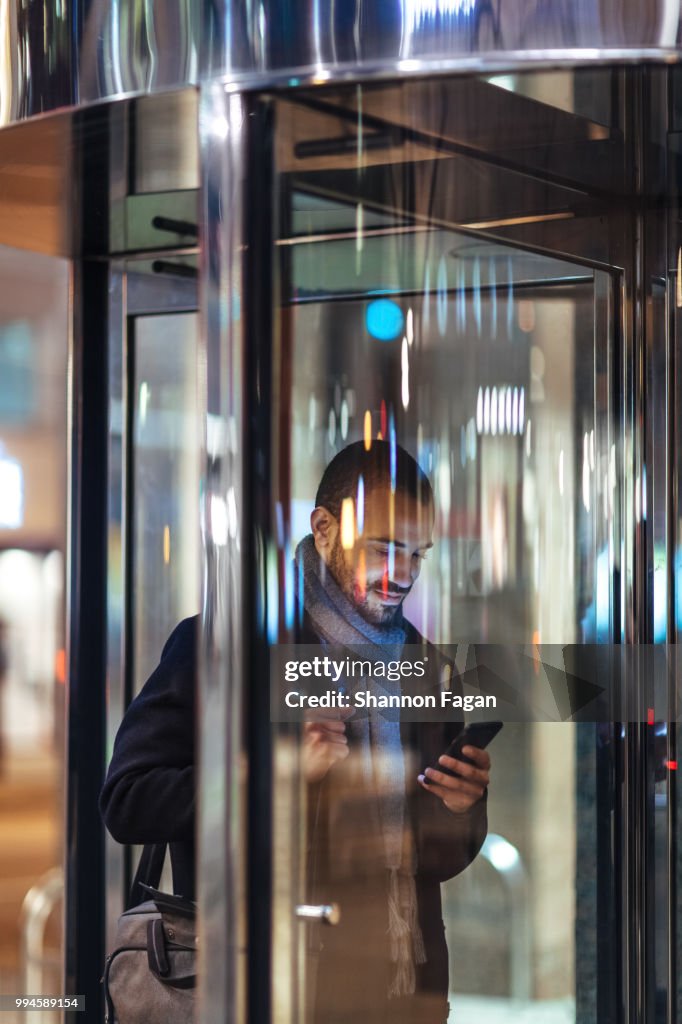 Young man with smart phone using revolving door