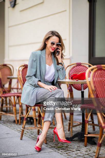 Alexandra Lapp sitting in a cafe talking on the phone wearing a checkered suit combination in black and white with a long blazer and high waist pants...