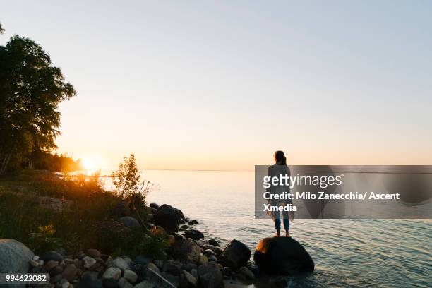 woman pauses on lakeshore at sunrise, looks off - michigan foto e immagini stock