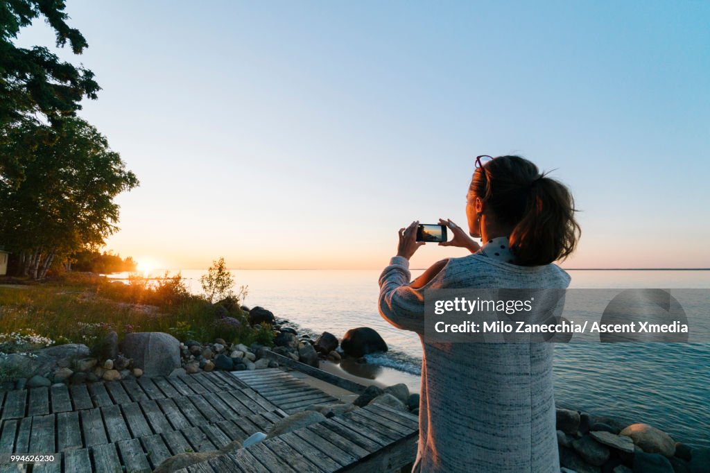 Woman pauses on lakeshore at sunrise, takes pic