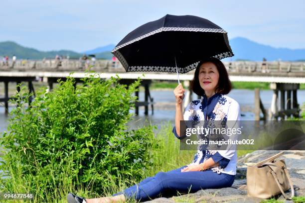京都嵐山のリバーサイドでリラックスした日本人女性 - 渡月橋 ストックフォトと画像