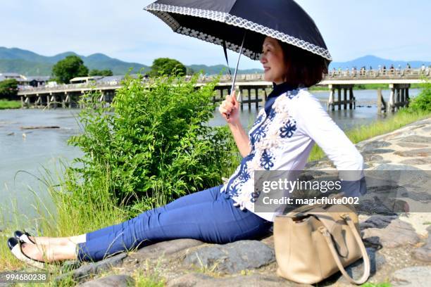 京都嵐山のリバーサイドでリラックスした日本人女性 - 渡月橋 ストックフォトと画像