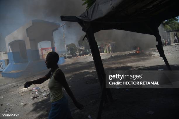 Women walks before a smouldering barricade in central Port-au-Prince, July 9 following two days of deadly looting and arson triggered by a...
