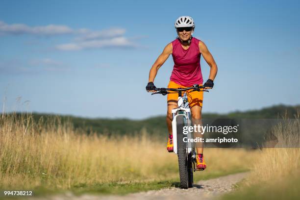 lächelnd 44 jahre alte frau radfahren mountainbike in ländlichen landschaft passen - 40 44 years stock-fotos und bilder