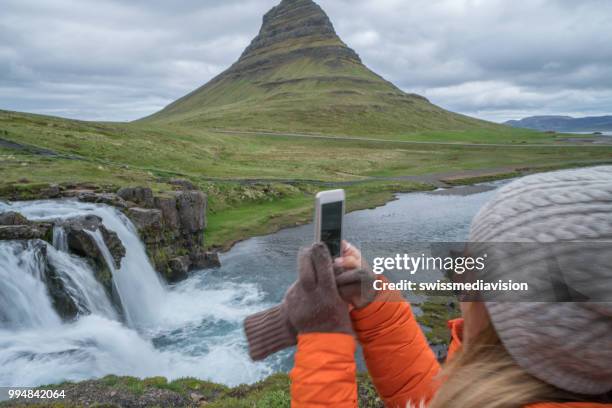 tourist female in iceland taking mobile phone picture of kirkjufell mountain - west central iceland stock pictures, royalty-free photos & images