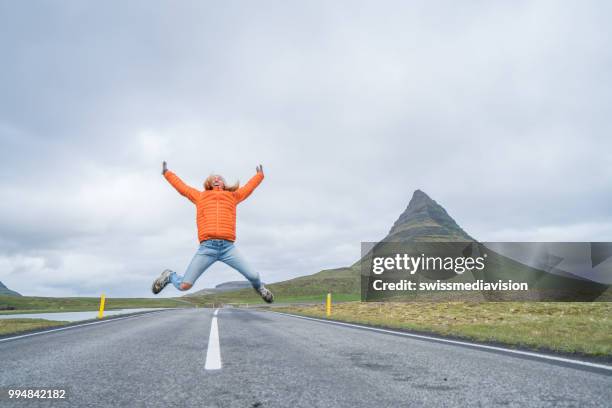 young woman in iceland jumping high up over road at famous kirkjufell mountain - west central iceland stock pictures, royalty-free photos & images