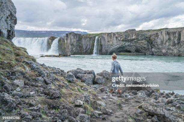 jonge vrouw overweegt waterval in ijsland - northeast iceland stockfoto's en -beelden