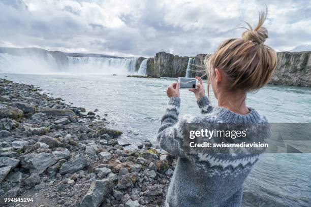 jonge vrouw nemen van mobiele telefoon foto bij waterval, ijsland - northeast iceland stockfoto's en -beelden
