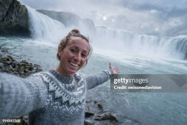 young woman taking selfie portrait with magnificent waterfall in iceland, godafoss falls. people travel exploration concept - myvatn stock pictures, royalty-free photos & images