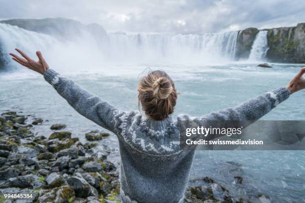 jonge vrouw armen gestrekt op spectaculaire waterval in ijsland - northeast iceland stockfoto's en -beelden