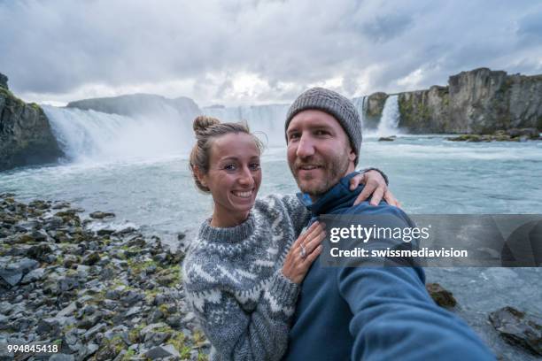 paar leuke selfie foto nemen door godafoss waterval op ijsland met smartphone te reizen. mensen bezoeken beroemde toeristische attracties en bezienswaardigheden op route 1 - northeast iceland stockfoto's en -beelden