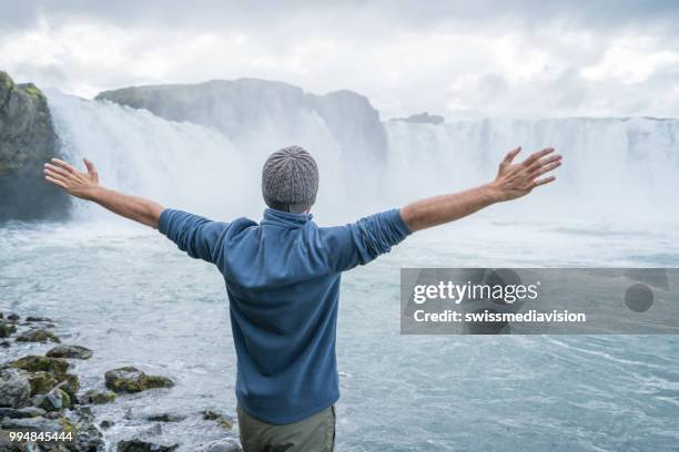 jonge man armen gestrekt op spectaculaire waterval in ijsland - northeast iceland stockfoto's en -beelden