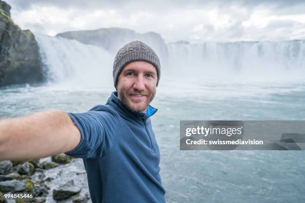 jonge man portretje van de selfie met prachtige waterval in ijsland, godafoss valt. mensen reizen exploratie concept - northeast iceland stockfoto's en -beelden