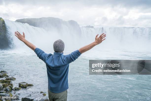 jonge man armen gestrekt op spectaculaire waterval in ijsland - northeast iceland stockfoto's en -beelden