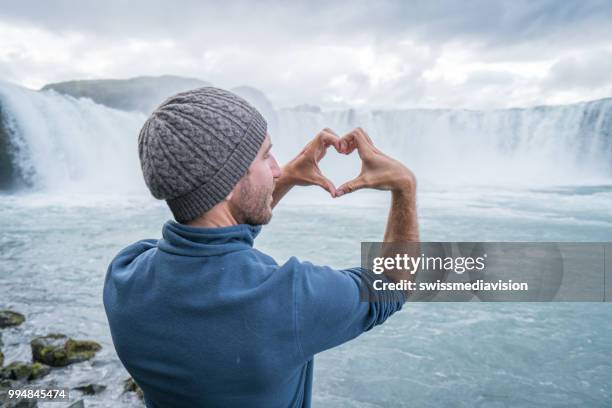 jonge man in ijsland hart vorm vinger frame op spectaculaire waterval maken - northeast iceland stockfoto's en -beelden