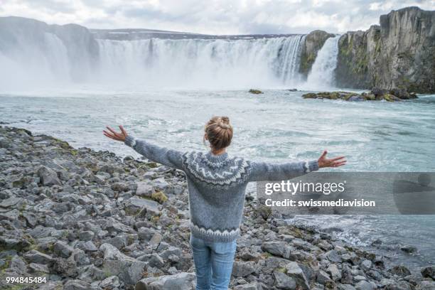 jonge vrouw armen gestrekt op spectaculaire waterval in ijsland - northeast iceland stockfoto's en -beelden