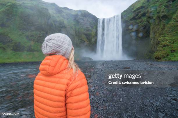 toeristische vrouwelijke reizen in ijsland staat in de buurt van de prachtige waterval en overweegt de natuur, mensen reizen avontuur concept - nationale snelweg stockfoto's en -beelden