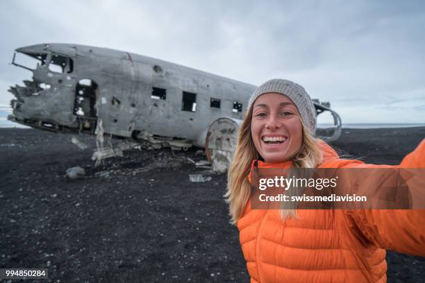 jonge vrouw permanent door vliegtuig wrak op zwarte zand strand een selfie portret bekende plaats om te bezoeken in ijsland en poseren met het wrak - nationale snelweg stockfoto's en -beelden