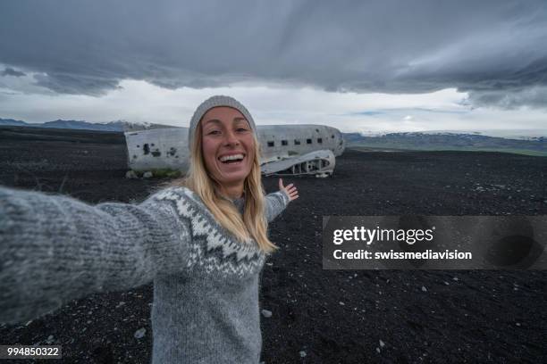 mädchen stehen durch flugzeug wrack am schwarzen sandstrand unter ein selfie porträts berühmter ort in island besuchen und stellen mit dem wrack - swissmediavision stock-fotos und bilder