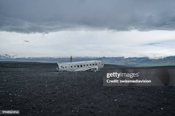 jeune homme se dresse sur l’avion s’est écrasée sur la plage de sable noir en parcourant son entourage envisage - swissmediavision photos et images de collection