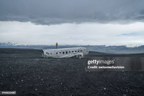 jeune homme se dresse sur l’avion s’est écrasée sur la plage de sable noir en parcourant son entourage envisage - swissmediavision photos et images de collection