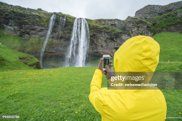 junge frau, die handy-aufnahme am wasserfall, island - swissmediavision stock-fotos und bilder