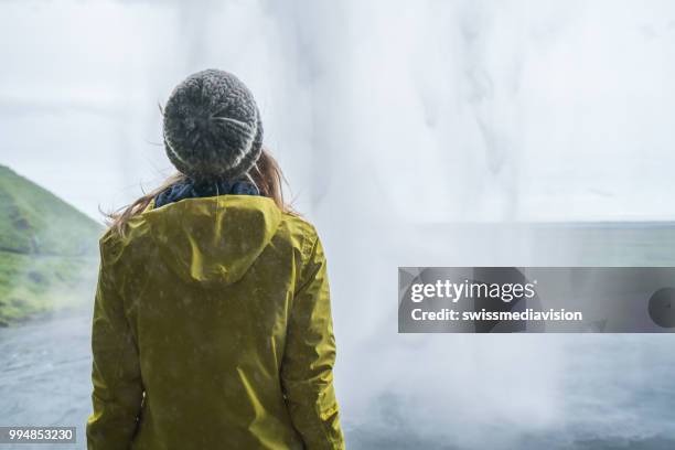 toeristische vrouwelijke reizen in ijsland staat achter de prachtige waterval en overweegt de natuur, mensen reizen avontuur concept - nationale snelweg stockfoto's en -beelden