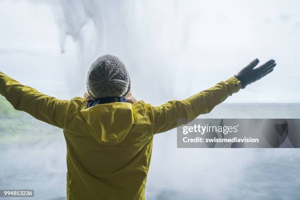 junge frau ausgestreckten hinter spektakulärer wasserfall in island - swissmediavision stock-fotos und bilder