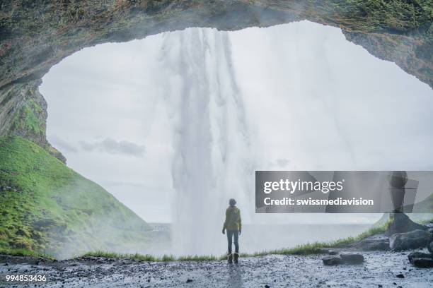 touristischen weibliche reisen in island steht hinter herrlichen wasserfall und betrachtet die natur, die leute reisen abenteuer-konzept - swissmediavision stock-fotos und bilder