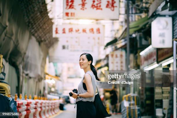 beautiful young woman carrying camera exploring and walking through local city street - chinese cultuur stockfoto's en -beelden