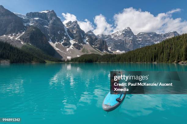 woman paddleboards across tranquil lake, mountains - technophiler mensch stock-fotos und bilder