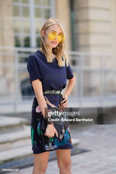 Leonie Hanne wears a dark blue Dior Evolution t-shirt, a black clutch, a flower print skirt, yellow glasses, outside Dior, during Paris Fashion Week...