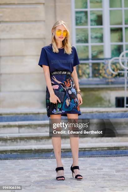 Leonie Hanne wears a dark blue Dior Evolution t-shirt, a black clutch, a flower print skirt, yellow glasses, outside Dior, during Paris Fashion Week...