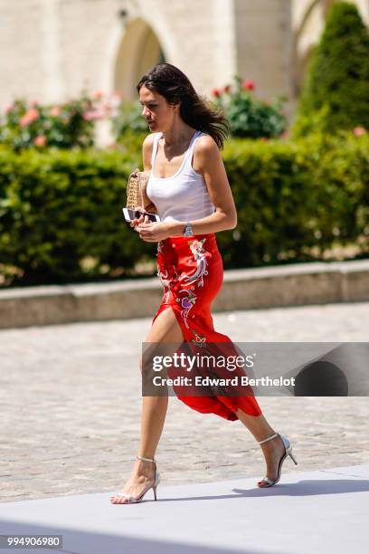 Guest wears a white sleeveless tank top, a red skirt with embroidered flowers, silver heels shoes , outside Dior, during Paris Fashion Week Haute...