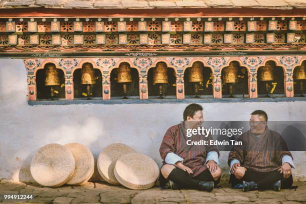 two bhutanese sitting on the ground of temple talk to each other happily - bhutan stock pictures, royalty-free photos & images