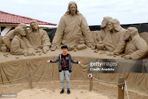 Boy poses for a photo in front of a sand sculpture along the Neva River in Saint Petersburg, Russia on July 09, 2018.