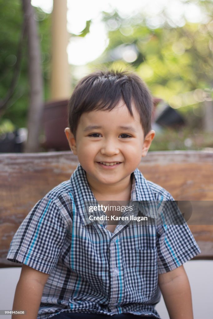 Outdoor portrait of cute toddler or preschool aged boy looking straight at camera and smiling