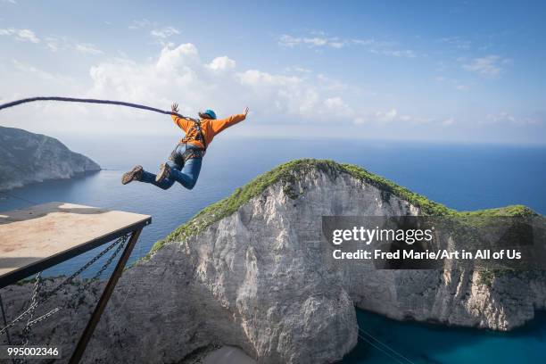 Members of the rope jump french team Pyrenaline jump from atop the rugged rocks overlooking the azure waters, Ionian Islands, Zakynthos, Greece.