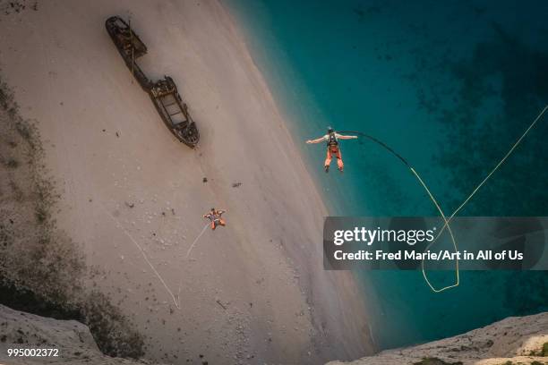 Members of the rope jump french team Pyrenaline jump from atop the rugged rocks overlooking the azure waters, Ionian Islands, Zakynthos, Greece.