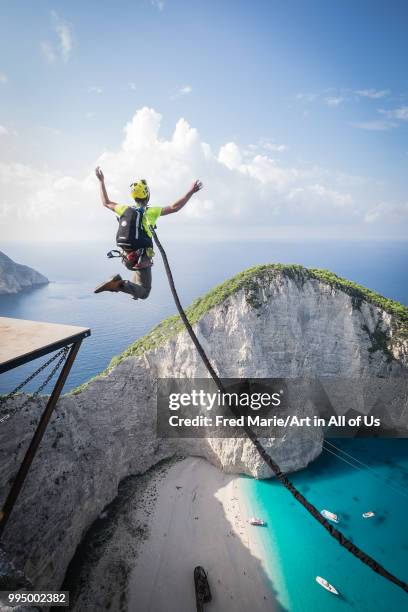 Members of the rope jump french team Pyrenaline jump from atop the rugged rocks overlooking the azure waters, Ionian Islands, Zakynthos, Greece.