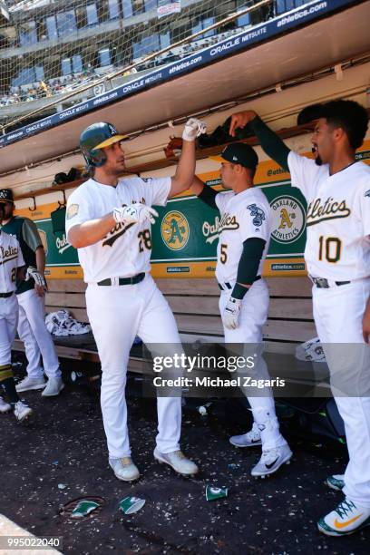 Matt Olson of the Oakland Athletics is congratulated in the dugout by Jake Smolinski and Marcus Semien after hitting a home run during the game...