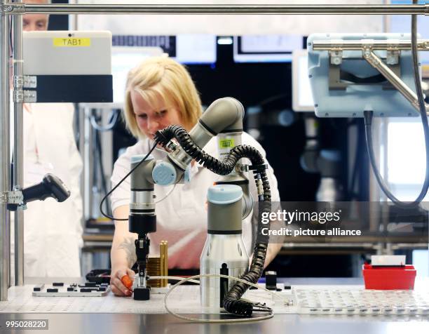 July 2018, Germany, Bocholt: The Gigaset employee Luisa Boeing and a robot assemble Gigaset's smartphone GS 185 in Bocholt. The company Gigaset is...