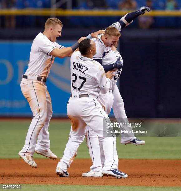 Daniel Robertson of the Tampa Bay Rays is congratulated on his game-winning hit by Jake Bauers and Carlos Gomez in the 10th inning of a baseball game...